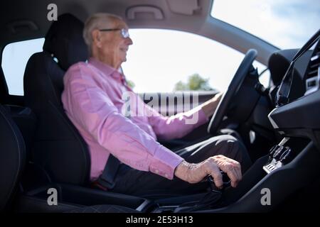 Interior Shot Of Smiling Senior Man Enjoying Driving Car With Hand On Gear Shift Stock Photo