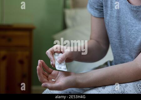Close Up Of Woman Sitting On Bed Wearing Pyjamas Taking Medication From Packet Of Pills Stock Photo