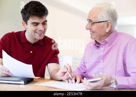 Young Man Helping Senior Neighbor With Paperwork At Home Stock Photo