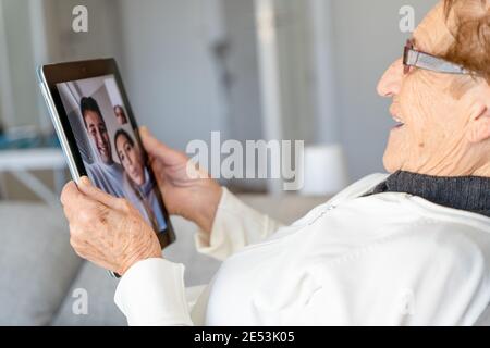 High angle side view of satisfied senior female resting on sofa at home and having video call with family while using table Stock Photo