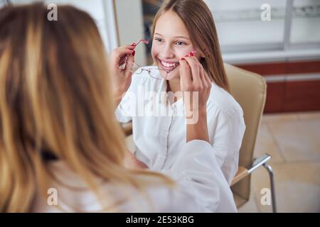 Happy friendly female child sitting in chair and choosing eyeglass in room indoors Stock Photo