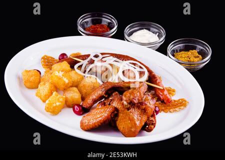 Large beer set of fried snacks - chicken wings, pork skewer, homemade sausages, potato chips, deep-fried cheese, onion, three sauces: white, red, must Stock Photo