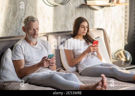 Man and woman with smartphones sitting on bed Stock Photo