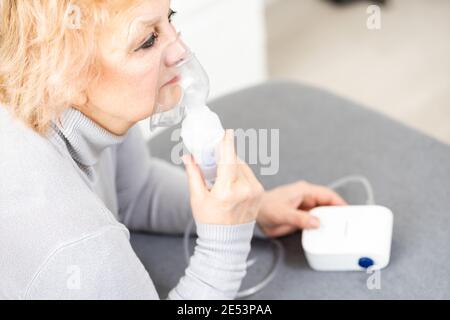 Elderly woman using asthma machine on light background Stock Photo