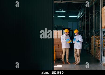 Two Caucasian workers discussing while younger worker holding documents. Warehouse interior. Stock Photo