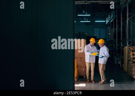 Two Caucasian workers discussing while younger worker holding documents. Warehouse interior. Stock Photo