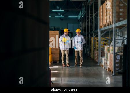 Cheerful father and son walking through their warehouse and talking about next steps in their business. Holding tablet and documents in their hands. Stock Photo