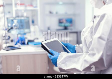 CLose up of medical researcher using tablet pc in laboratory dressed in ppe. Team of scientists conducting vaccine development using high tech technology for researching treatment against covid19 Stock Photo
