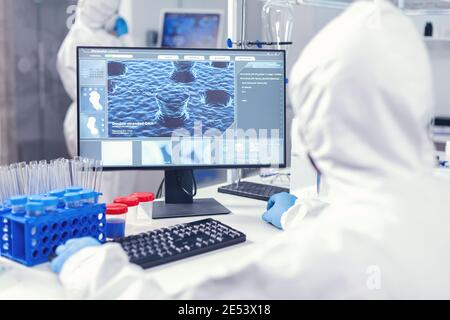 Over the shoulder shot of scientist monitoring and working with coronavirus dressed in ppe. Lab engineers conducting experiment for vaccine development against covid19 virus. Stock Photo