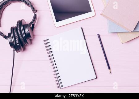 Study at home flat lay composition with blank notepad and pencil among books, tablet PC and headphones on pink wooden table, top view. Stock Photo
