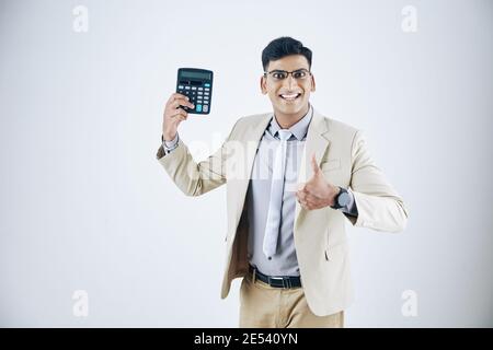 Happy excited young entrepreneur with calculator in hand showing thumbs-up and looking at camera, isolated on white Stock Photo