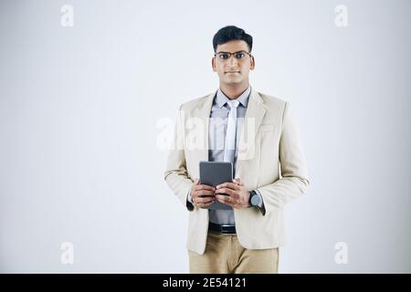 Portrait of confident serious young Indian businessman in glasses holding tablet computer and looking at camera Stock Photo