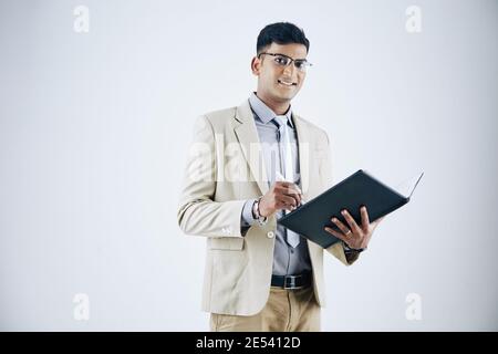 Studio portrait of handsome young Indian businessman taking notes in document Stock Photo