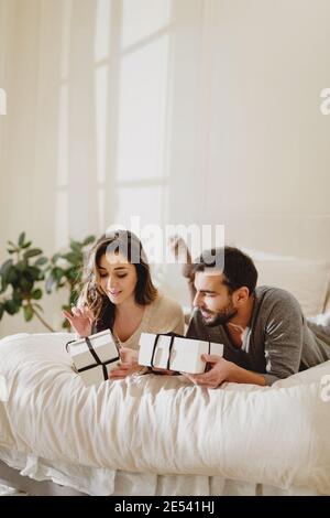 Beautiful couple in love lying in the bed and make a present to each other on Valentine's Day. Stock Photo