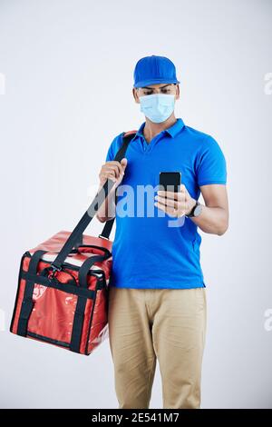 Serious delivery man in protective mask checking customer address in mobile application where he should deliver food Stock Photo