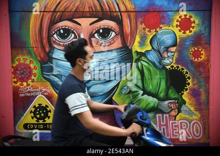 (210126) -- TANGERANG, Jan. 26, 2021 (Xinhua) -- A man wearing face mask rides past a mural saluting frontline workers at a neighborhood in Tangerang, Banten province, Indonesia, Jan. 26, 2021. (Xinhua/Zulkarnain) Stock Photo