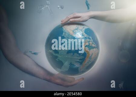 Women's and men's hands support the globe of planet Earth. Around the flying plastic debris. The concept of preserving the earth's environment. Light. Stock Photo