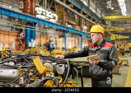 Worker in helmet using tablet pc and examining machine equipment in the plant Stock Photo