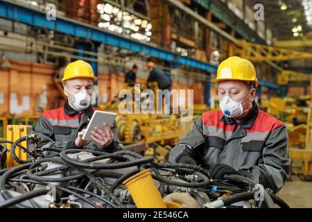 Two workers in masks Working in team with machine equipment in the plant Stock Photo