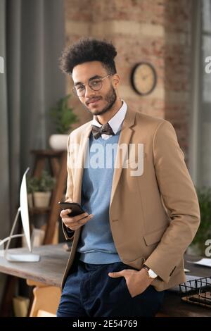 Portrait of young man with stylish hairstyle looking at camera while using his mobile phone Stock Photo