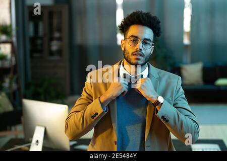 Portrait of young man in eyeglasses looking at camera wearing bow tie to his stylish suit while standing at office Stock Photo