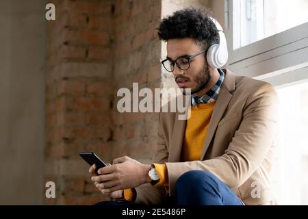 Young man in wireless headphone using his mobile phone to listen to music Stock Photo