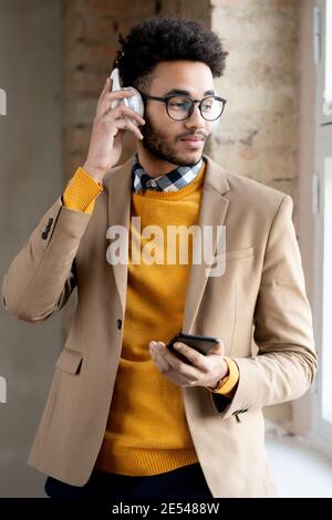 Young man in headphones looking through the window and listening to music on his mobile phone Stock Photo
