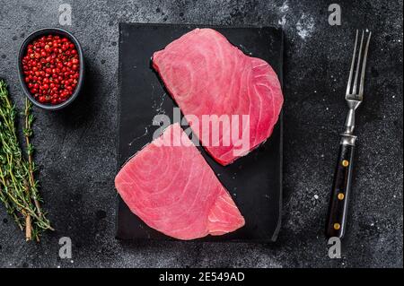Raw tuna steak on a marble cutting Board . Black background. Top view Stock Photo