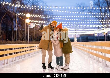 Happy family making selfie portrait on mobile phone while skating on ice rink Stock Photo
