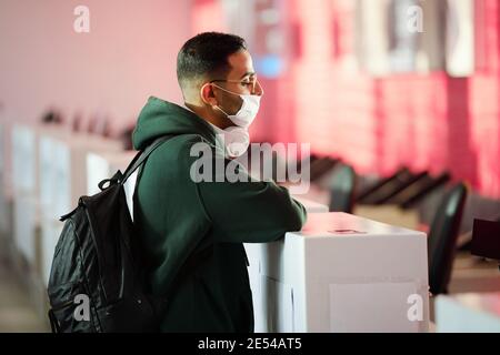 Young man in protective mask standing at the registration desk at the airport Stock Photo