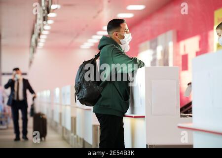 Man in protective mask with backpack behind his back standing at reception desk at the airport Stock Photo
