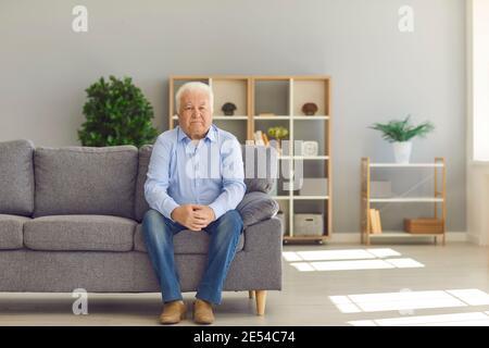 White-haired senior man sitting alone on couch at home and thinking about his life Stock Photo
