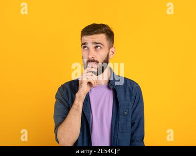 Portrait of pensive young bearded man touching his chin, deep in thought over orange studio background Stock Photo