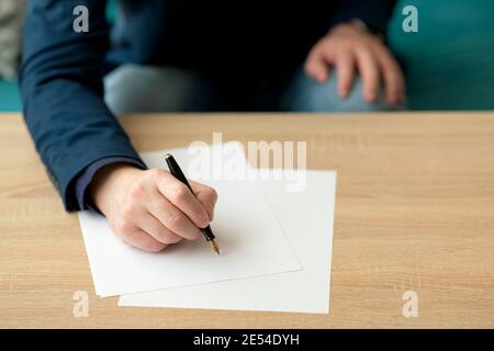 Businessman in the office writes a letter or signs a document on a piece of white paper with a fountain pen with nib Stock Photo