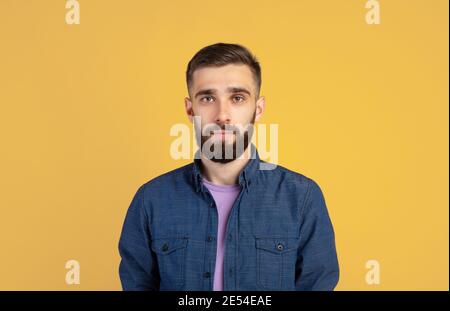 Portrait of charismatic bearded young man in casual clothes looking at camera over orange studio background Stock Photo