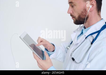 Young serious male doctor in earphones pointing at digital tablet while taking online patients and giving them medical recommendations Stock Photo
