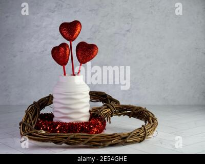 Valentine’s Day decor, a wooden heart wreath, red glittery heart wreath and a white vase filled with 3 red glittery hearts sticking up on a herringbon Stock Photo