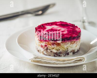 Layered salad herring under fur coat on table. Portion of traditional russian salad with herring, beet and other vegetables on white linen tablecloth. Copy space Stock Photo