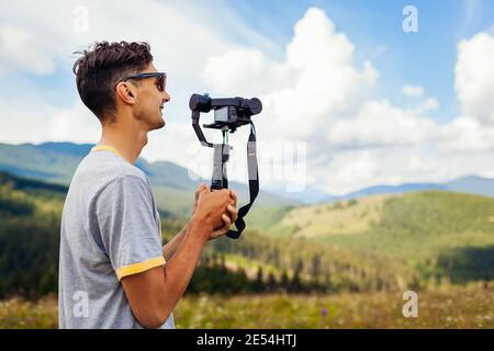 Videographer filming Carpathian mountains landscape. Man using steadicam and camera to make footage. Video shoot. Traveling wtih digital devices Stock Photo