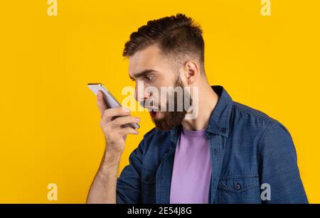 Angry bearded guy shouting at smartphone over orange studio background, panorama Stock Photo