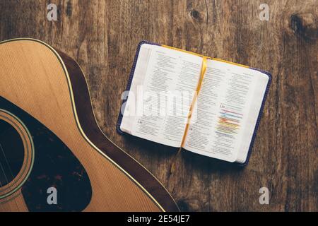 A guitar and a open bible on a wooden background in a dimly lit environment. Soft light and worship Stock Photo