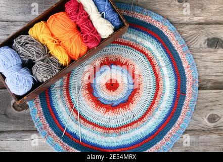 Knitted striped mat and colorful skeins of wollen yarn on wooden background. Stock Photo