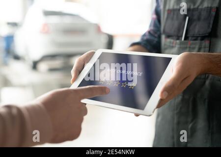 Hands of car maintenance center technician holding digital tablet with five stars on display while client going to rate the service after repairing Stock Photo