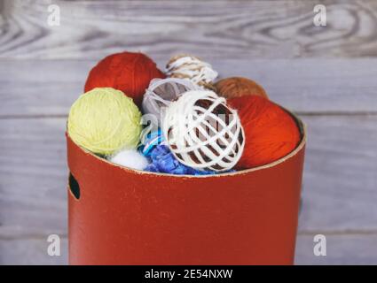 Colorful balls of yarn in round box on wooden wall background. Knitting or crocheting yarn. Stock Photo