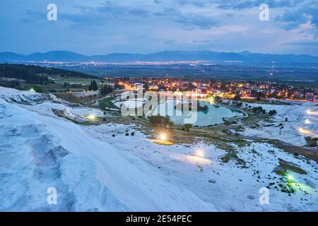 Pamukkale travertines in foreground. Sunset sky and illuminated houses in background. Stock Photo