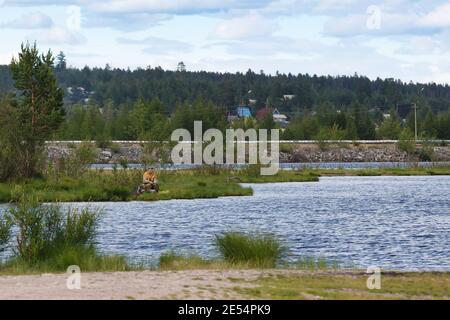 Neryungri District, Yakutia, Russia. July 13, 2016 A man is fishing in a pond against the backdrop of a forest and houses. Stock Photo
