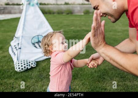 Father and a son giving a high five to each other outside in a garden. Cheerful toddler boy having fun with his father on a sunny summer day. Stock Photo