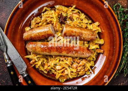 Bigos Stewed cabbage with mushrooms and meat sausages on a plate. Dark background. Top view Stock Photo