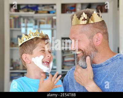 Father and son put the crown on their heads and have fun. Father has a beard. Son made a beard out of shaving foam Stock Photo
