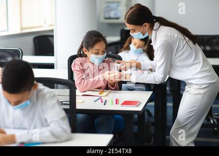 Teacher applying antibacterial sanitizer on pupil's hands Stock Photo